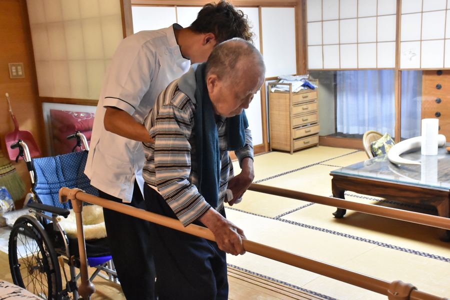自宅の和室で、手すりを使って立つ練習をする様子