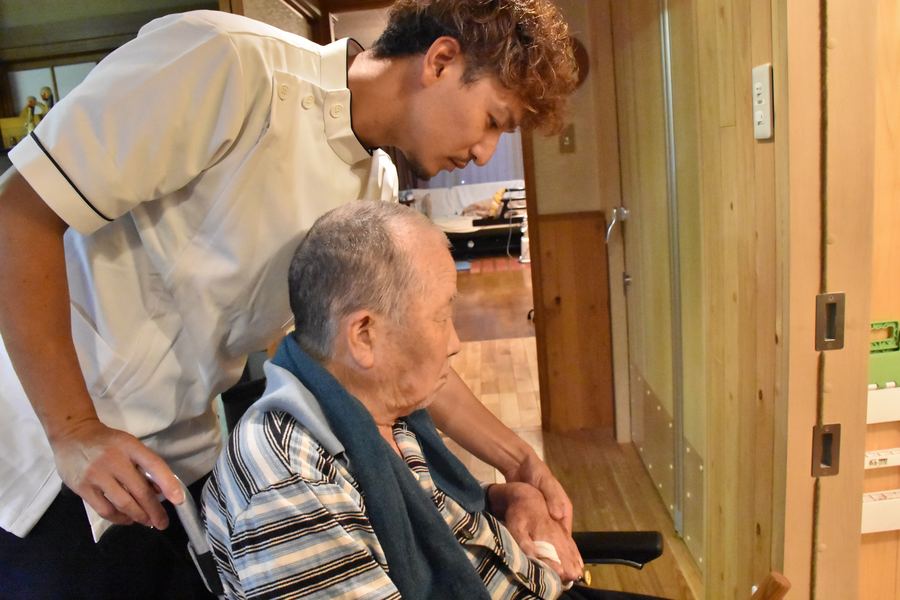 車いすの男性に寄り添い、手の動きを確かめるセラピスト